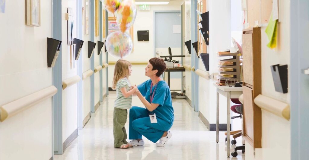 A Nurse Talking To A Child In A Hallway Of A Hospital