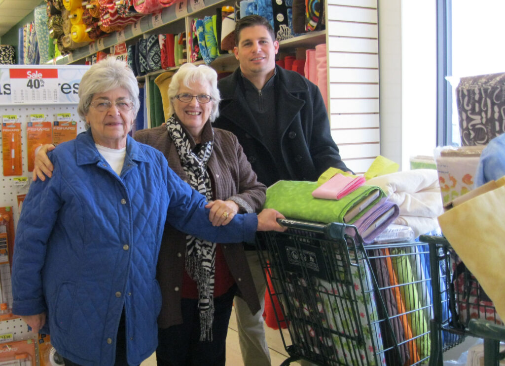 Three People At A Fabric Store Purchasing Materials To Make Quilts